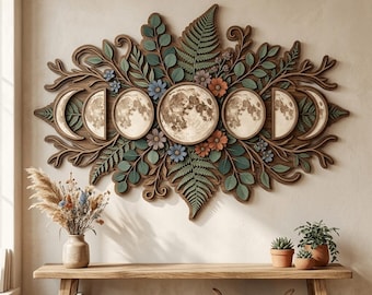 Puede incluir: Una pieza de arte mural horizontal de madera que presenta una luna llena central rodeada de fases lunares, intrincadamente superpuesta con hojas de helecho verdes, ramas de eucalipto y pequeñas flores azules y naranjas.