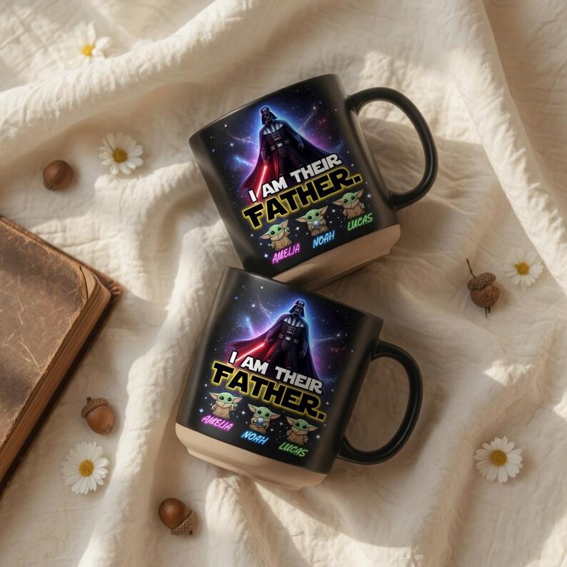 May include: Two black ceramic mugs with a Star Wars theme. Each mug features Darth Vader, the text "I AM THEIR FATHER," and three Baby Yoda characters with the names Amelia, Noah, and Lucas. The mugs have a beige base and black handle.