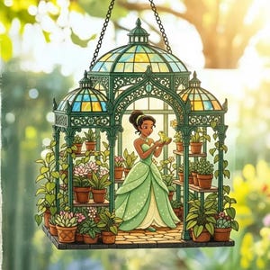 May include: A decorative hanging ornament depicting a cartoon woman in a green dress holding a frog within a greenhouse. The greenhouse has a green frame, stained glass roof, and is filled with potted plants. The ornament is suspended from a chain.