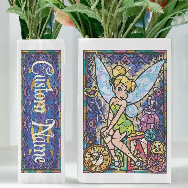 May include: Two white ceramic vases with a stained-glass design. One vase features the text "Custom Name" in gold lettering. The other vase has a colorful image of Tinkerbell from Peter Pan. The vases are filled with greenery.