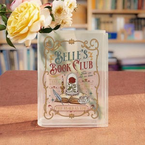 Può includere: Custodia per libri in plastica trasparente con la scritta "Belle's Book Club" e una rosa in una cupola di vetro. Il design include una piuma, una tazza da tè e una candela. La custodia è decorata con bordi ornati e le parole "Tale as old as time."
