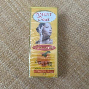 May include: A yellow box of Piment Doux skin care product. The box features the brand name, a woman's face, and a picture of a pumpkin. The text "CONCENTRÉ" and "Unifiant & Clarifiant AUX ACIDES DE FRUITS" are also visible.