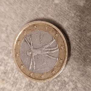 May include: A silver and gold colored Euro coin with a depiction of a man in a circle with stars around the edge.