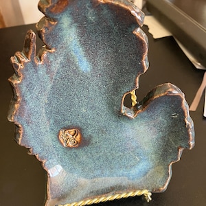 May include: A ceramic outline of the state of Michigan in a teal blue glaze with a gold stand. The outline has a brown glaze on the edges and a gold heart with the word "Love" inside.