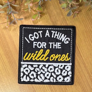 May include: Black square patch with white stitching and the text "I GOT A THING FOR THE wild ones" in white and yellow. The bottom of the patch has a white and black leopard print design.