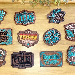 May include: A collection of ten embroidered patches featuring brown faux leather backgrounds with turquoise and black stitching. Designs include floral motifs, a steer skull, feathers, and text such as Texas, Bless Your Heart, Yeehaw Cowboy, Country Girl at Heart, My Pen Is Huge, Beautiful Crazy, and Just a Small Town Girl.
