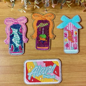 May include: Four embroidered patches with the word "Alani" in a cursive font. The patches feature bow designs and colorful illustrations of watermelon, candy apples, and floral patterns. The patches are on a wooden surface.