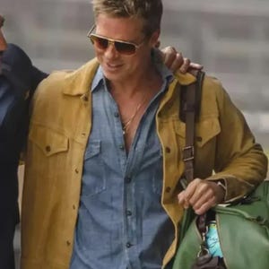 Puede incluir: Un hombre con una chaqueta amarilla mostaza sobre una camisa vaquera azul, gafas de sol con montura dorada y una cadena de oro. Lleva una bolsa de lona verde con una correa marr&oacute;n. La imagen es un plano medio con fondo borroso.