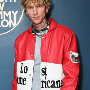 May include: Red and white leather jacket with the text "Lost Americana" on the front. The jacket has a patch on the sleeve with an American flag design. The jacket is worn over a light blue shirt.