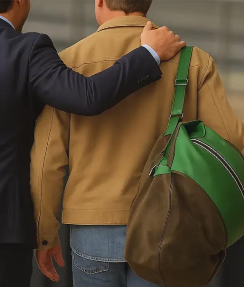Puede incluir: Se ven una chaqueta color canela, vaqueros azules y una bolsa de lona verde y marr&oacute;n. Una persona con un traje azul marino tiene el brazo alrededor de la persona que lleva la chaqueta color canela. La bolsa de lona tiene una correa verde.