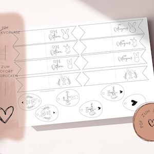 May include: A white printable PDF sheet with Easter-themed designs. It includes banners with "Frohe Ostern" and "Ostergruss" text, bunny illustrations, and egg-shaped tags with Easter greetings and bunny designs.