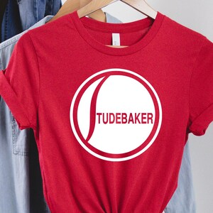 May include: Red t-shirt with a white circle and the text "Studebaker" inside the circle.
