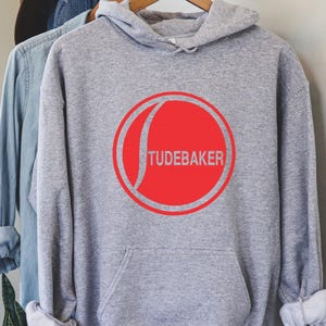 May include: Grey hooded sweatshirt with a red circle logo that says "TUDEBAKER" in white text.