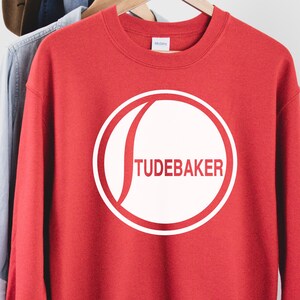 May include: Red sweatshirt with a white circle logo that says "TUDEBAKER" on it.