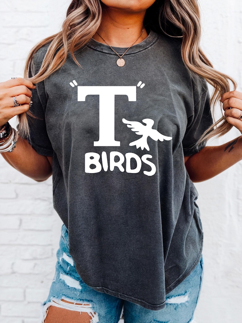 以下が含まれることがあります： 白い「T BIRDS」の文字と様式化された鳥のグラフィックが特徴の、濃い灰色のTシャツ。 ヴィンテージ感のあるウォッシュ加工で、半袖です。 カジュアルなユニセックスTシャツ。