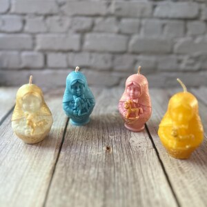May include: Four decorative candles in a row, each with a unique design. The candles are in shades of yellow, blue, and pink, with a white brick background. The candles are shaped like figures and have wicks.