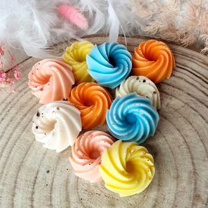 Peut inclure: Assortiment de fondants de cire en forme de spirale de couleurs vives dans des tons de bleu, jaune, orange et rose. Les fondants de cire sont disposés sur une surface en bois.