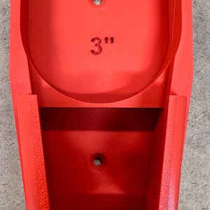 May include: A bright red, 3D-printed holder with a curved top and a rectangular base. The holder features a 3-inch measurement printed on the front. It has two holes for mounting.
