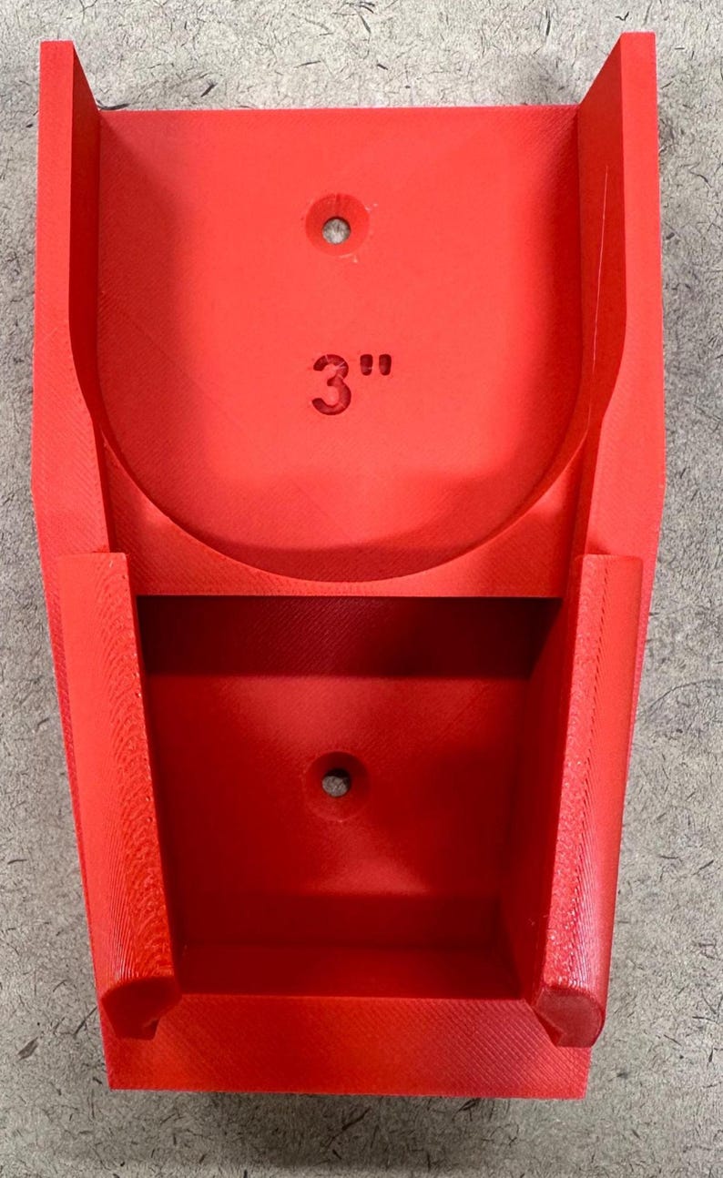 May include: A bright red, 3D-printed holder with a curved top and a rectangular base. The holder features a 3-inch measurement printed on the front. It has two holes for mounting.