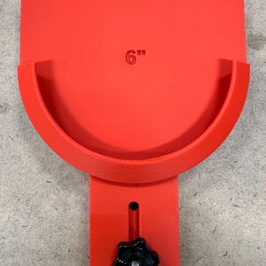 May include: A bright red tool with a 6-inch measurement marking. The tool features a curved section and a rectangular base with a black star-shaped knob. The tool is designed for a specific purpose.