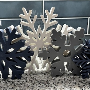 以下が含まれることがあります： 青、グレー、白の様々な色合いの4つの装飾的な雪の結晶のセット。テキスト「Set 1」が表示されています。これらの冬をテーマにした装飾は、休日のディスプレイに最適です。
