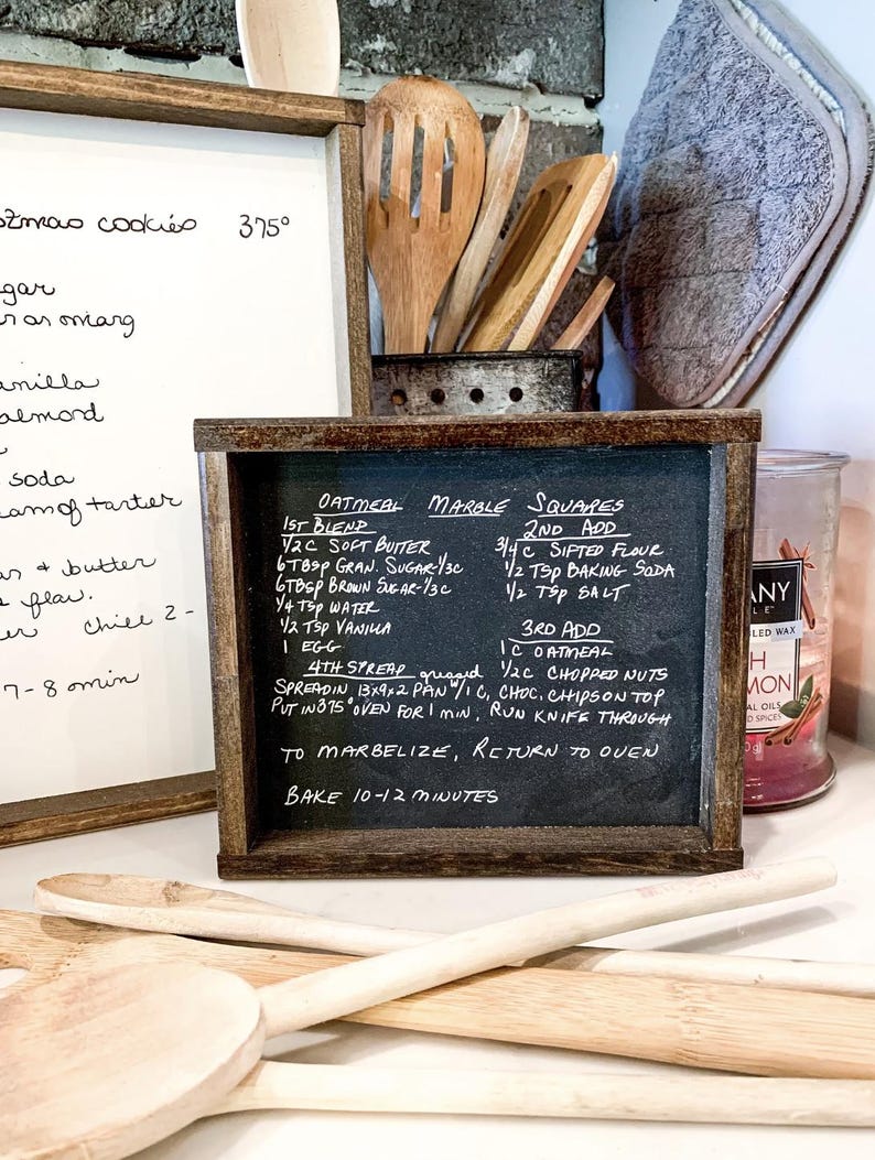 May include: A chalkboard sign with a handwritten recipe for Oatmeal Marble Squares. The recipe includes ingredients and instructions for baking the squares. The sign is framed in dark wood and has a rustic look.