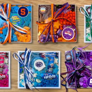 May include: Several white boxes filled with colorful candies, each tied with a ribbon. The boxes contain various candies, including gummy worms, star-shaped candies, and hard candies. Some boxes have university logos.