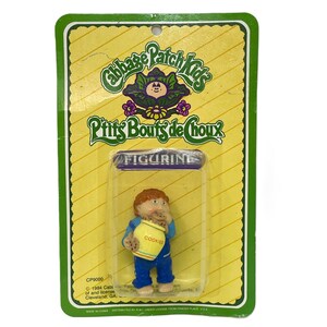 May include: A vintage Cabbage Patch Kids figurine on its original packaging. The figurine is of a child holding a cookie jar. The packaging has the words "Cabbage Patch Kids" and "P'tits Bouts de Choux" printed on it.