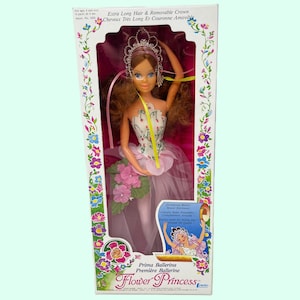 May include: A boxed Prima Ballerina Flower Princess doll. The doll features long brown hair, a removable crown, and a pink and white floral dress. The box is decorated with flowers and the text reads "Extra Long Hair & Removable Crown."