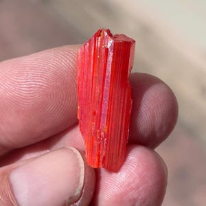 Könnte beinhalten: Ein leuchtend orangefarbener Kristall mit einer gestreiften Textur. Der Kristall ist lang und dünn, mit einer spitzen Spitze.