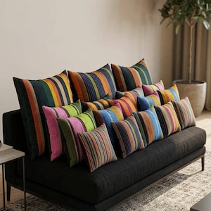 May include: A black sofa is decorated with a selection of vibrant, striped cushions. The cushions display a range of colours, including green, orange, blue, pink, and yellow. The sofa is placed on a patterned rug.