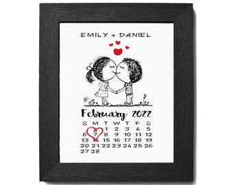 May include: A black framed print with a white background featuring a cartoon couple kissing with the text "EMILY + DANIEL" and a calendar for February 2022 with a red heart on the 7th.