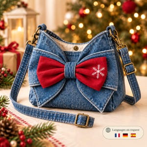 Può includere: Una borsa a tracolla in denim blu con un grande fiocco in tessuto rosso sul davanti. Il fiocco è decorato con un motivo a fiocco di neve ricamato in bianco. La borsa include una tracolla regolabile in denim con finiture in ottone anticato.