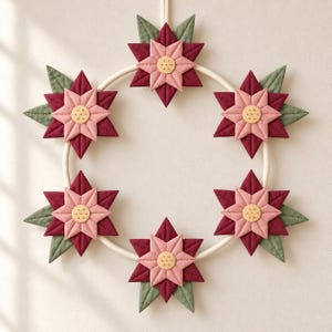 Op de afbeelding: Een ronde krans met zes gewatteerde stoffen bloemen gerangschikt rond een witte ring. Elke bloem bestaat uit gelaagde bordeauxrode en lichtroze stervormige bloemblaadjes met een lichtgeel centrum en groene bladeren als accenten.