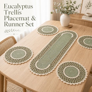 May include: A crochet placemat and runner set in sage green and cream. The set includes one long oval runner and four round placemats, each featuring a solid center and a decorative openwork border. Text reads: Eucalyptus Trellis Placemat & Runner Set.