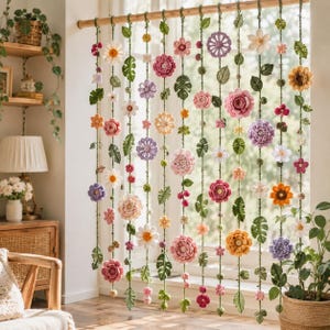 May include: A decorative hanging room divider featuring multiple vertical strands of crocheted flowers and green leaves in various shapes and colors, suspended from a wooden rod. The floral elements include roses, daisies, and sunflowers.