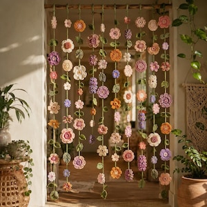 May include: A hanging room divider featuring multiple vertical strands of crocheted flowers in various colors including pink, orange, purple, and white, interspersed with green crocheted leaves, suspended from a horizontal wooden rod.