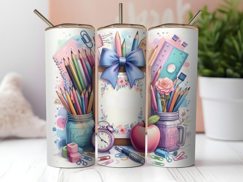 May include: A white tumbler with a gold lid and straw, featuring a watercolor design of school supplies. The design includes pencils, a ruler, an apple, and a blue bow. The tumbler is decorated with a jar of pencils and a pink flower.