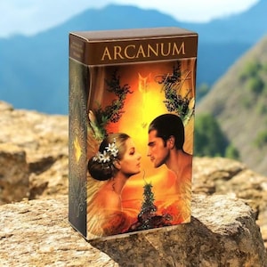 May include: A rectangular box with the word "ARCANUM" on top. The box features a romantic illustration of a man and woman facing each other, with a warm, golden background. The box is set against a natural, outdoor backdrop.