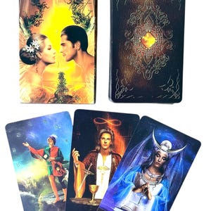 May include: A tarot card deck with the word "ARCANUM" on the box. The box features a couple in a romantic embrace. Three tarot cards are displayed, including "The Fool" and "The High Priestess". The card backs have an ornate design.