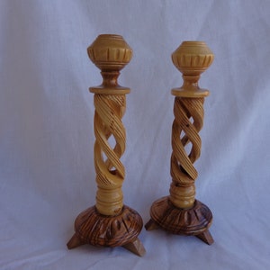 May include: A pair of wooden candle holders with a spiral design. The candle holders are made of light brown wood and have a natural finish.