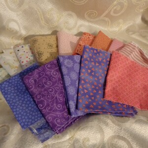 May include: A collection of fabric squares in various shades of purple, pink, and beige with different patterns. The fabrics are arranged in a fan shape.