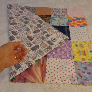 May include: A patchwork quilt with various fabric patterns, including cats, flowers, and polka dots. The quilt is partially folded, revealing a cat-themed fabric. The quilt is made of multiple squares of different colors and designs.