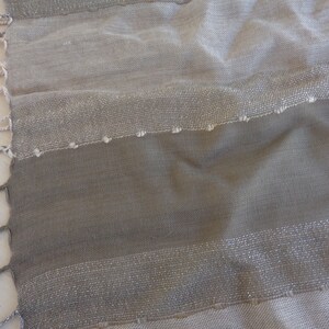 May include: A close-up of a beige and brown striped scarf with a silver thread woven into the fabric. The scarf has a fringe on the edges.