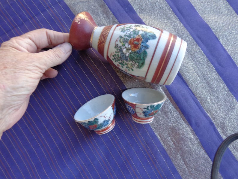 two cups and sake container Enlarge for detail Vintage Sake set Signed Scene has flower on one side and Four Japanese Men on other