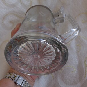 May include: A clear glass beer stein with a pewter lid and a handle. The bottom of the stein has a decorative, starburst pattern.