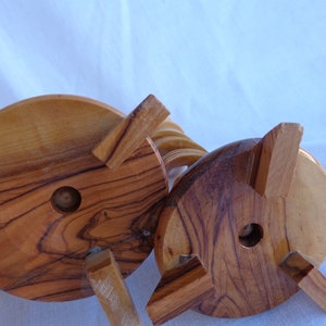 May include: The underside of a wooden candle holder with a spiral design. The base is made of natural wood with a light brown color and a circular shape. The holder has four legs that are attached to the base.