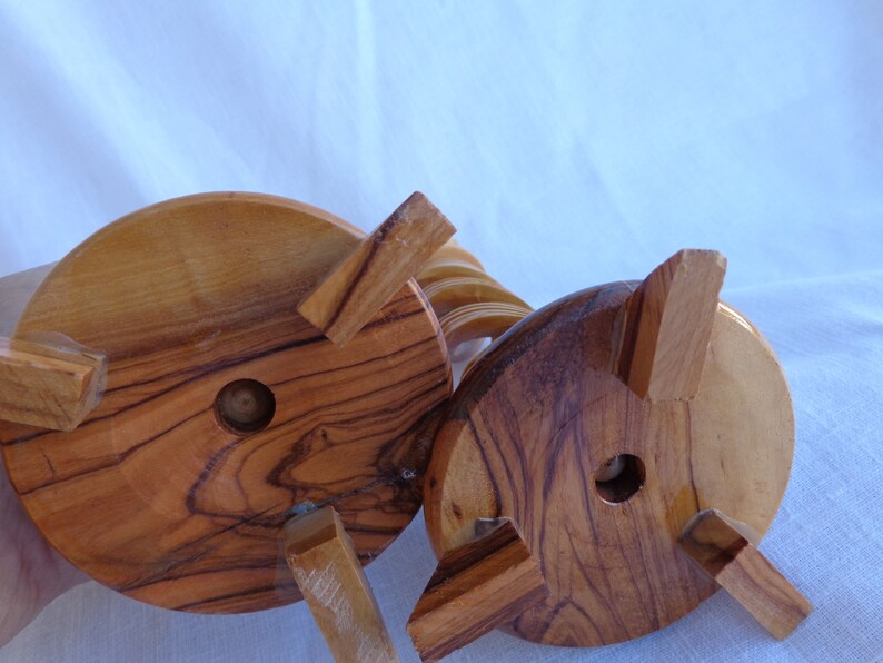 May include: The underside of a wooden candle holder with a spiral design. The base is made of natural wood with a light brown color and a circular shape. The holder has four legs that are attached to the base.