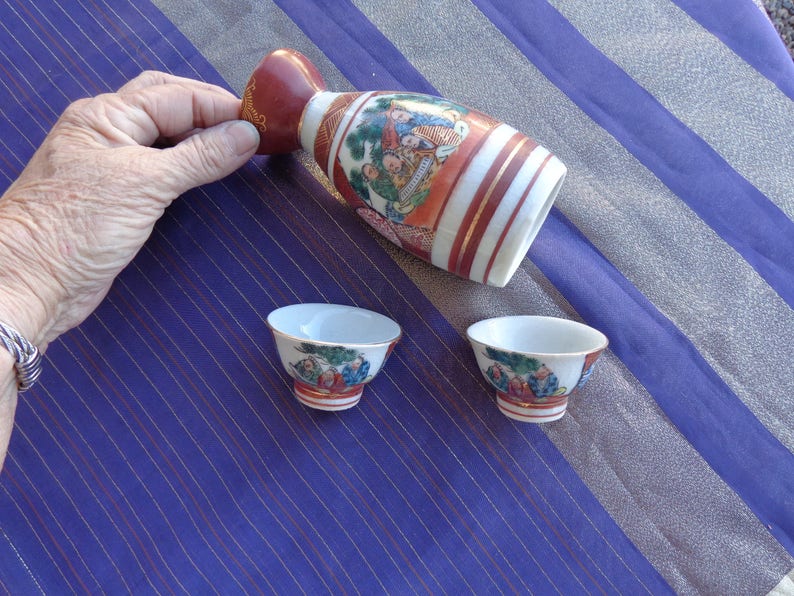 two cups and sake container Enlarge for detail Vintage Sake set Signed Scene has flower on one side and Four Japanese Men on other