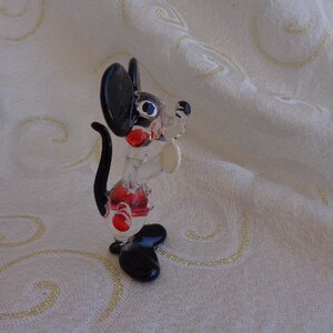 May include: A black and white glass figurine of a cartoon mouse with red accents. The mouse is standing on its hind legs with its tail curled behind it.